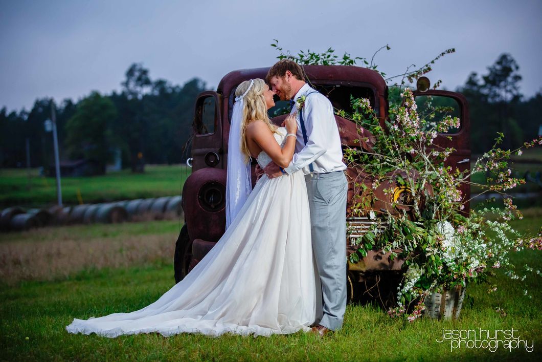 Bride and groom embracing beside an old red truck covered in greenery